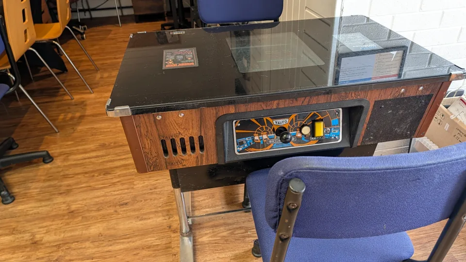 A glass-topped cocktail arcade cabinet with a chair beside it